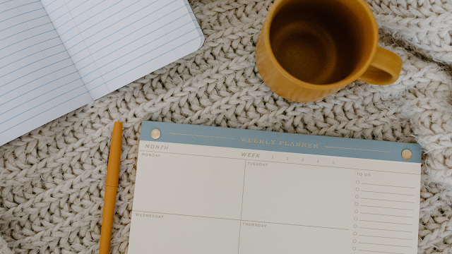 Planner semanal, caderno e caneca sobre manta de lã — organização, rotina e autocuidado no dia a dia.