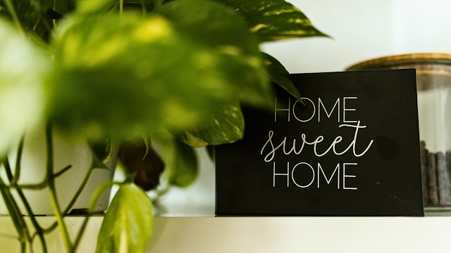 Placa decorativa com a frase "Home Sweet Home" ao lado de plantas verdes, simbolizando conforto e bem-estar em casa.