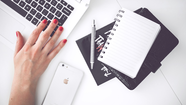 Secretária branca com portátil, caderno e telemóvel, representando organização digital e produtividade