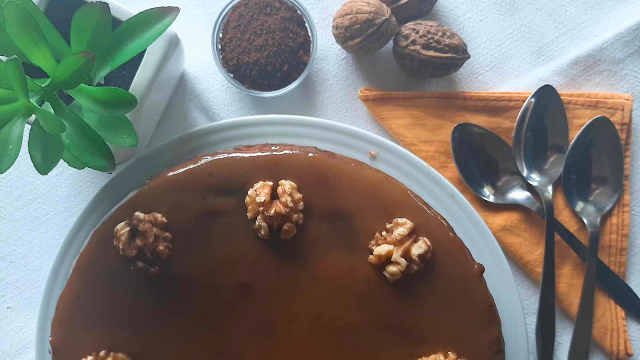 Bolo cremoso decorado com nozes, por cima, nozes, e café solúvel, uma planta e colheres, a simbolizar um momento de tranquilidade