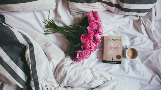 Flores, livro e café na cama Buquê de flores cor-de-rosa, livro 'Me Before You' e chávena de café sobre lençóis brancos, criando um ambiente acolhedor e relaxante