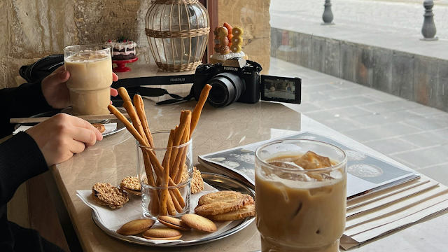 Mesa de café com bolachas, grissinis e café gelado ao lado de uma câmara fotográfica, simbolizando momentos inspiradores e criativos de janeiro.