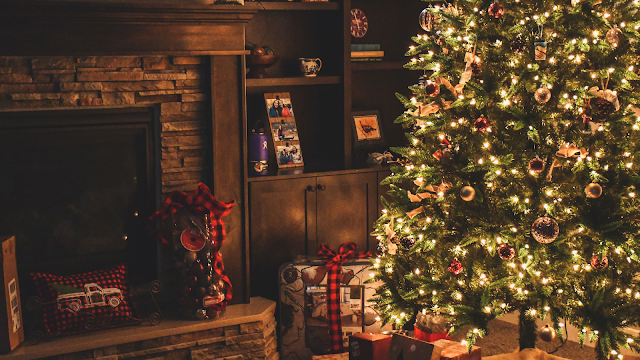 Sala acolhedora com árvore de Natal iluminada, presentes com laços vermelhos e lareira decorada, representando o espírito natalício tradicional.