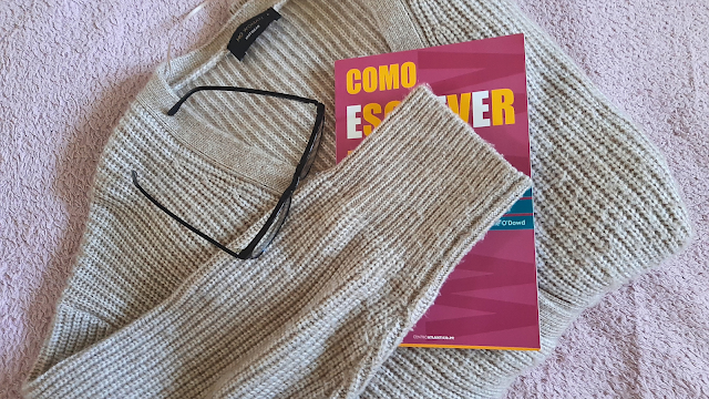 Imagem de uma camisola, um livro aberto e óculos sobre uma superfície, criando um ambiente aconchegante e perfeito para uma leitura relaxante.