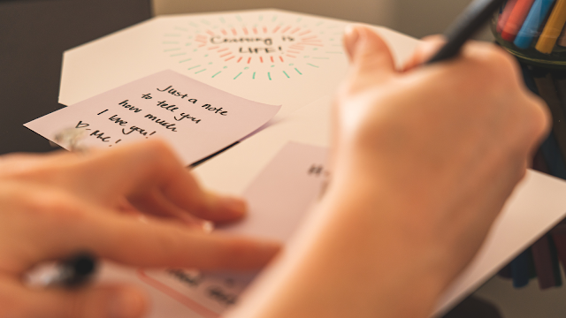 Mãos a escrever uma carta em papel, representando o exercício de escrita criativa e reflexão sobre metas futuras e autoconhecimento.
