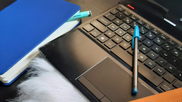 Computador, canetas coloridas e bloco de notas sobre uma mesa, simbolizando organização e produtividade no trabalho.