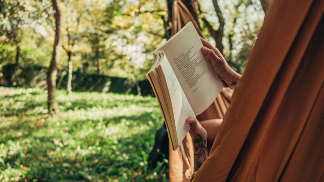 Pessoa deitada numa cama de rede a ler um livro, espaço verde ao redor, simbolizando momentos de descanso.