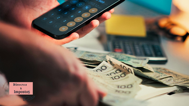 Alterações fiscais em 2026 e impacto no orçamento familiar Mão a segurar um telemóvel com calculadora aberta, notas de euro sobre a secretária e uma calculadora ao fundo, representando o impacto das alterações fiscais no orçamento familiar.