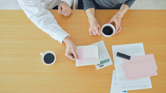 Duas pessoas sentadas a uma mesa a analisar documentos e faturas, com uma calculadora e chávenas de café, num momento de organização financeira.