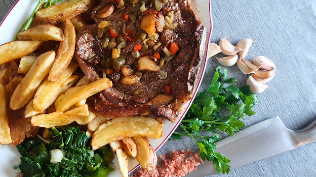 Bife ao alho suculento servido numa travessa, acompanhado por alhos, salsa fresca e uma faca de sal ao lado