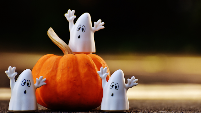 Fantasmas decorativos ao lado de uma abóbora laranja, ideia criativa de decoração para o Halloween.