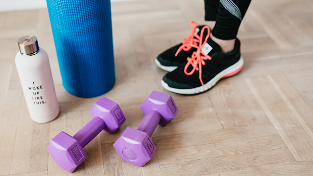 Exercício físico em casa com material simples Halteres, tapete de yoga, sapatilhas e garrafa de água no chão, representando atividade física em casa de forma simples e acessível.