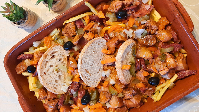 Travessa de pica-pau tradicional com carne salteada, enchidos, pickles, azeitonas pretas e batatas fritas, servida com fatias de pão rústico.