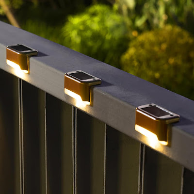 Close-up de três pequenas luzes solares instaladas no topo de um corrimão metálico à noite. As luzes emitem um brilho quente e suave, criando um efeito de iluminação elegante e acolhedor para espaços exteriores, como terraços ou varandas.