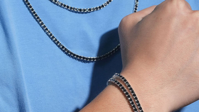 Homem a usar pulseira e colar masculinos prateados com pedras pretas, combinados com t-shirt azul clara
