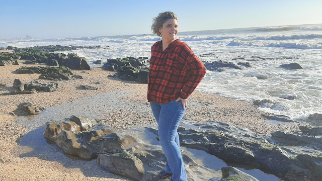 Teresa Isabel Silva na praia, refletindo sobre a importância de pausar e encontrar inspiração na natureza para despertar a criatividade e inovação no dia a dia.