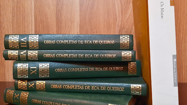 Coleção de volumes encadernados das Obras Completas de Eça de Queiroz empilhados sobre uma mesa, ao lado do livro Os Maias — fotografia ilustrando artigo sobre o autor português.