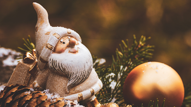Estatueta do Pai Natal entre pinhas e ramos de pinheiro, simbolizando o espírito natalício e a perda da magia do Natal.