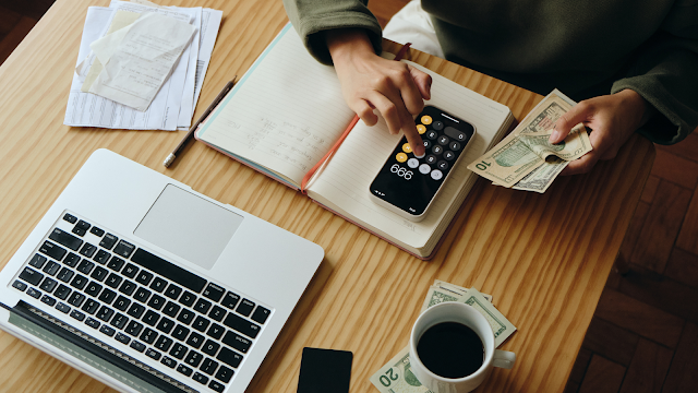 Pessoa a calcular despesas com dinheiro, recibos e computador portátil em cima da mesa, representando a gestão financeira e o apoio à renda Porta 65 em Portugal.