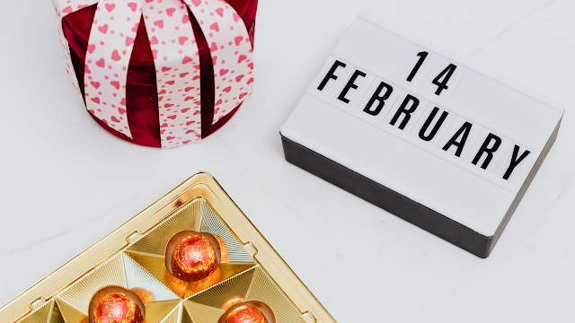 4 de Fevereiro: O Dia dos Namorados em Imagem Caixa de luz com a data 14 de fevereiro, chocolates dourados e uma prenda decorada com fitas de corações, representando o Dia dos Namorados.