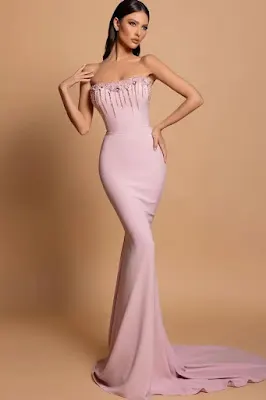 Vestido Longo Sereia Rosa com Decote Tomara que Caia e Pedraria Modelo a posar de corpo inteiro em estúdio, vestindo um vestido longo estilo sereia na cor rosa claro, com decote tomara que caia e aplicações de pedraria e franjas de cristais no corpete.