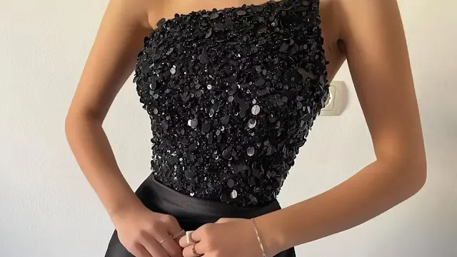 Woman wearing an elegant black one-shoulder dress, with a bodice fully covered in sparkling sequins and a lower section made of black satin fabric.